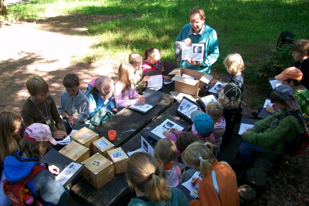 Kindergruppe arbeitet im Wald mit Erdsch&uuml;tzer-Ordnern und Bastelmaterialien am Tisch
