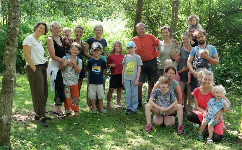 Gruppe von Eltern und Kindern steht gemeinsam lachend im Grünen, umgeben von Bäumen und Natur.